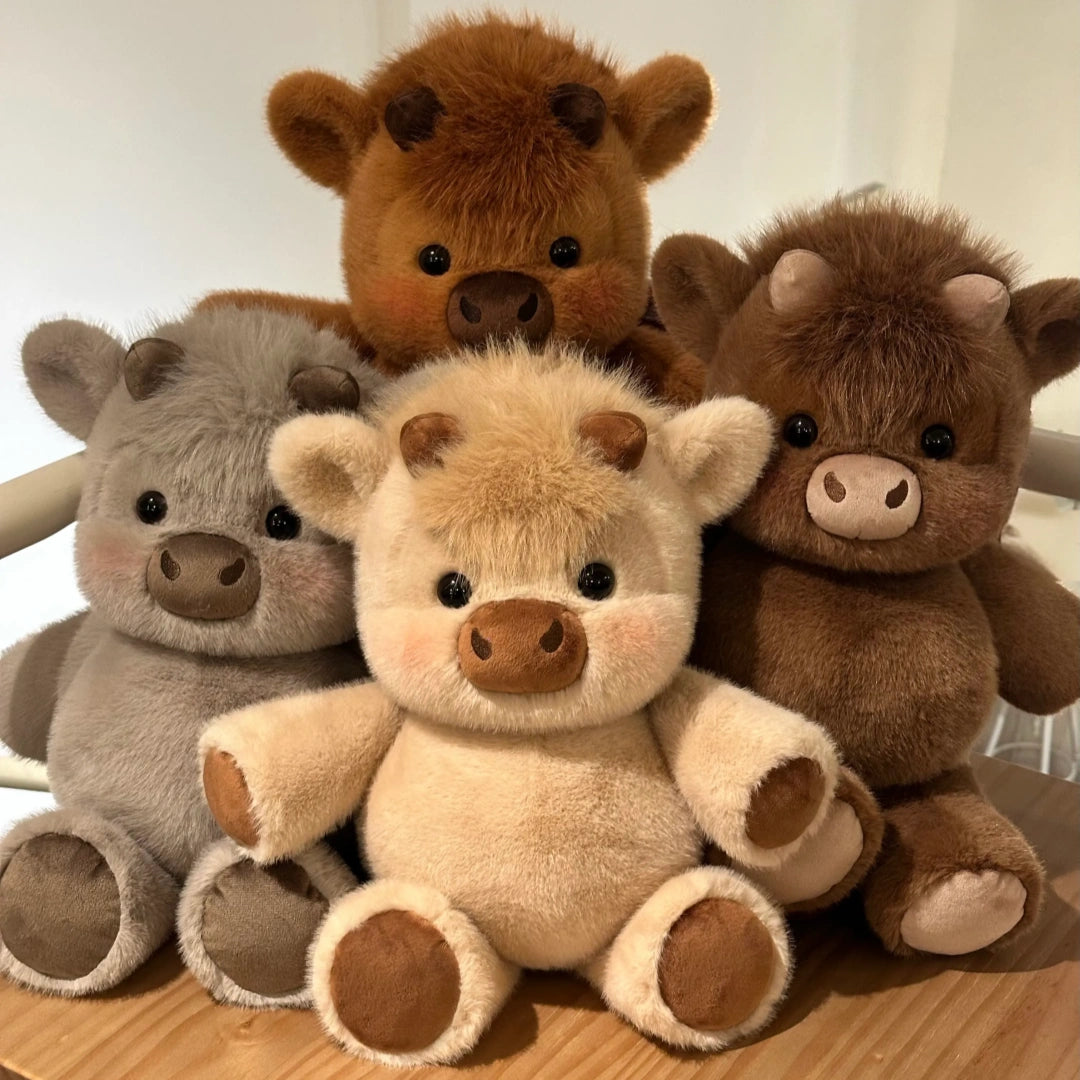 Four plush toy animals arranged together on a wooden surface against a light indoor background. The set includes a gray pig, a cream cow, a medium brown cow, and a dark brown calf.